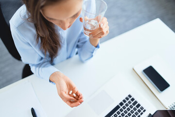 Overhead view of woman taking painkillers while sitting on office - obrazy, fototapety, plakaty