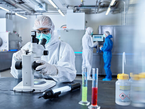 Chemists working in industrial laboratory, wearing protective clothing, using microscope