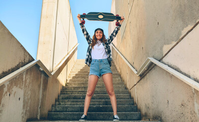 Portrait of happy young woman standing on staircase holding up her longboard