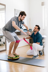 Physiotherapist assisting patient, practicing on balance trainer
