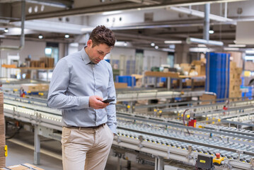 Man at conveyor belt in factory looking at cell phone