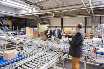 Three businessmen at conveyor belt in factory