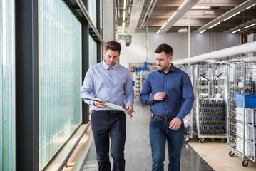 Two men walking in factory shop floor talking about product