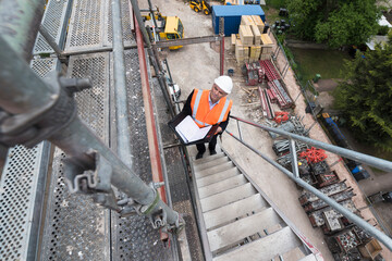 Man wearing safety vest on scaffolding on construction site - obrazy, fototapety, plakaty