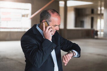 Businessman on cell phone in building under construction checking the time