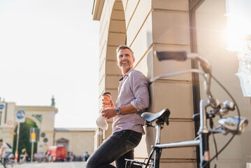 Obraz premium Smiling man with bicycle and takeaway coffee in the city