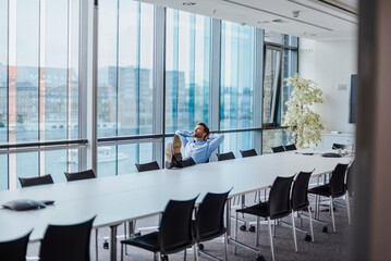 Germany, Berlin, businessman sitting in conference room with feet up looking out of the window