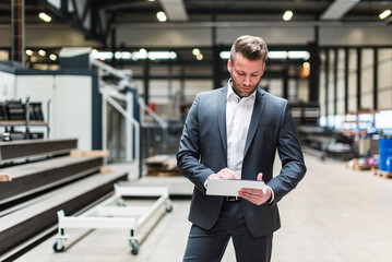 Businessman with tablet standing on factory shop floor