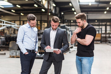 Three men sharing tablet on factory shop floor