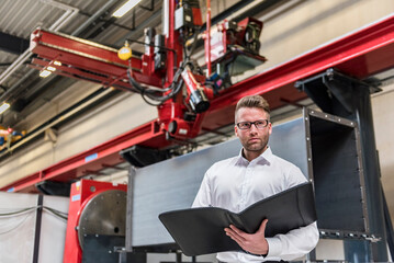 Businessman with folder standing on factory shop floor