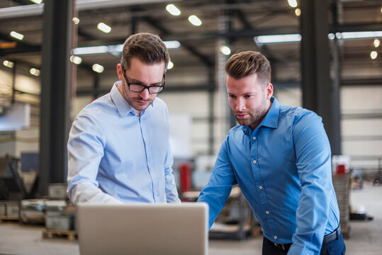 Two businessmen sharing laptop on factory shop floor