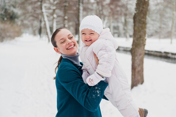 Portrait of happy baby girl having fun with her mother in snow-covered landscape