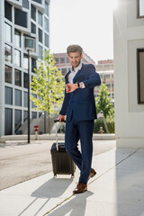 Businessman with baggage in the city on the move checking the time