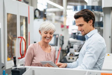 Smiling businessman and senior woman with tablet talking in a factory - Powered by Adobe