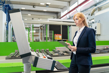 Businesswoman using tablet at machine in factory