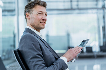 Businessman sitting in waiting area using tablet