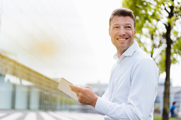 Smiling businessman with tablet outside in the city