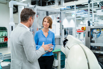 Businessman with tablet and woman talking at assembly robot in a factory