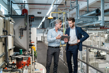 Two businessmen with tablet talking in a modern factory - obrazy, fototapety, plakaty