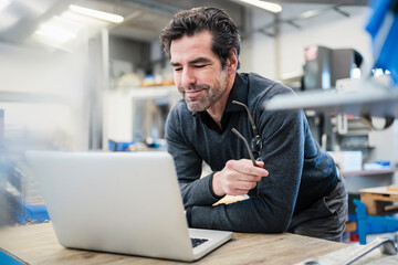 Businessman using laptop in a factory - obrazy, fototapety, plakaty