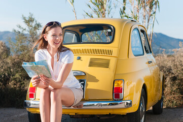 Portrait of laughing woman with map sitting on bumper of yellow vinage car, Sardinia, Italy - obrazy, fototapety, plakaty
