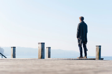 Man looking at lake against clear sky while standing on pier during sunny day