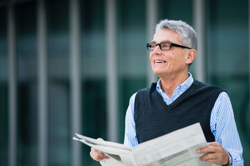 Portrait of smiling senior businessman with newspaper outdoors