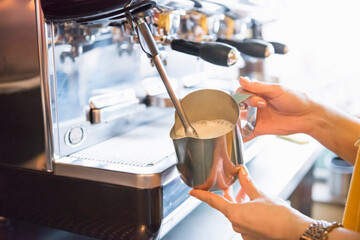 Hands of female barista frothing milk with espresso machine in coffee shop