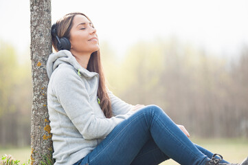 Relaxed woman listening music while leaning on tree trunk at park