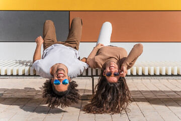 Couple with sunglasses, relaxing on bench, lying on back, heads hanging down