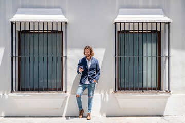 Smiling young male entrepreneur using smart phone while standing amidst windows