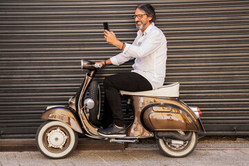 Happy mature man taking selfie while sitting on motor scooter against black shutter
