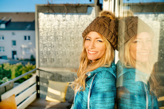 Portrait of smiling blond mature woman wearing bobble hat on balcony