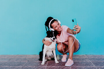 Happy woman taking selfie with Border Collie dog against turquoise wall