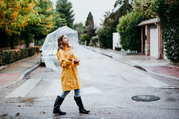 Smiling girl in raincoat holding umbrella while walking on road in city