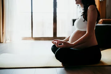 Selbstklebende Fototapeten Pregnant woman meditating while sitting on exercise mat at home © tunedin