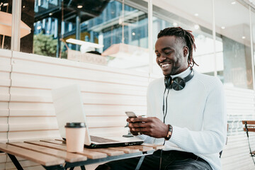 Smiling creative businessman with laptop using mobile phone in cafe