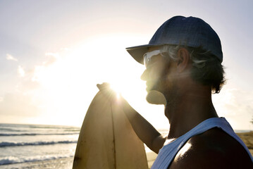 Man with surfboard watching sunset on the beach