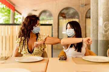 Young women wearing masks while greeting with elbow bump in restaurant
