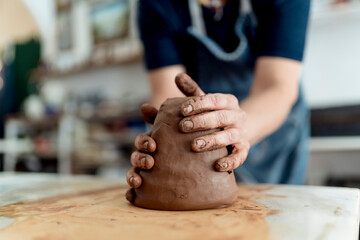 Female artist molding a shape from brown clay in crafts workshop