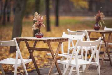 Autumn outdoor terrace with wooden table, chairs and decorations. Autumnal street scene in park with fallen leaves. Street view of a coffee terrace with tables and chairs in europe. - obrazy, fototapety, plakaty