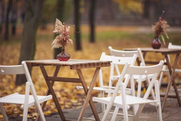 Foto auf Acrylglas Autumn outdoor terrace with wooden table, chairs and decorations. Autumnal street scene in park with fallen leaves. Street view of a coffee terrace with tables and chairs in europe. © Cristina