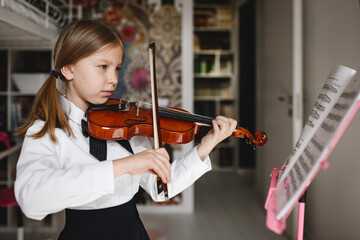 Girl playing violin looking at music stand at home