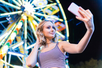 Portrait of teenage girl taking selfie in front of big wheel at fair