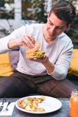 Young man sitting on couch in a restaurant having a vegan burger for lunch
