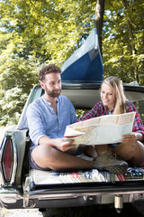 Smiling young couple with map and canoe in car at a brook
