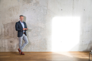 Businessman with cell phone leaning against concrete wall in a loft