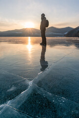 A hiker in winter clothes stands on a frozen ice surface. The mirror-smooth surface of lake ice and...