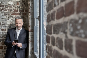 Businessman at a brick wall checking cell phone