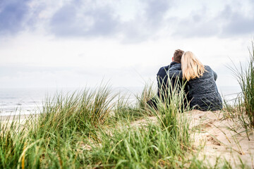 Couple sitting in dunes - obrazy, fototapety, plakaty